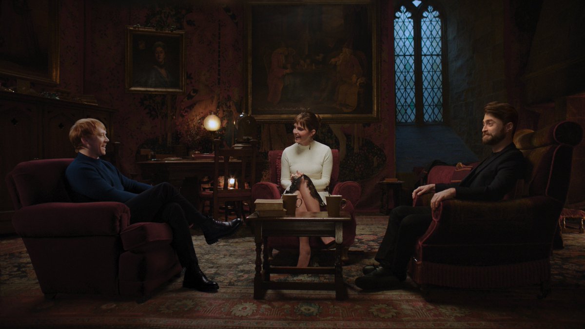 Rupert Grint, Emma Watson, and Daniel Radcliffe sit around a table in armchairs in the Gryffindor common room