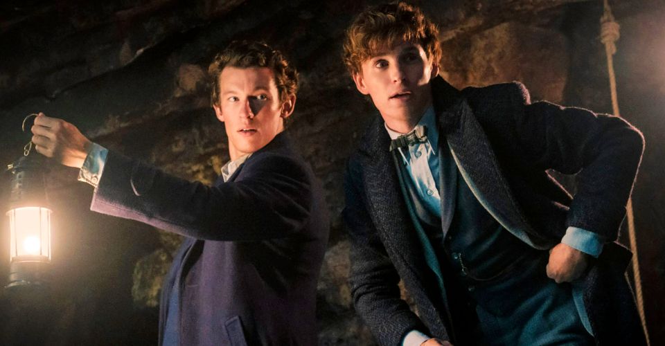 Newt Scamander (played by Eddie Redmayne) and Theseus Scamander (played by Callum Turner) are pictured mid-adventure in a cave. Theseus is holding a lantern and Newt looks ready to spring into action.