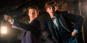 Newt Scamander (played by Eddie Redmayne) and Theseus Scamander (played by Callum Turner) are pictured mid-adventure in a cave. Theseus is holding a lantern and Newt looks ready to spring into action.