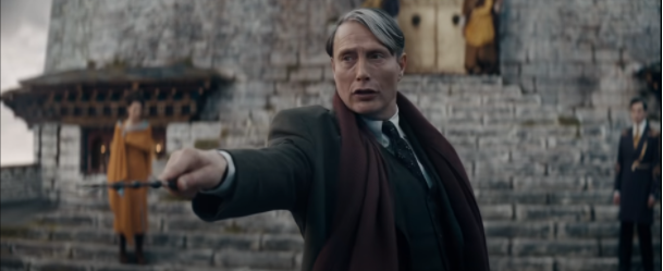 Gellert Grindelwald stands in front of a stone building, pointing his wand in front of him, in a still from the trailer for Fantastic Beasts: The Secrets of Grindelwald