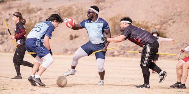 There is a one chaser holding a chaser, chaser from oponent's team is trying to hold him. In front of him is one beater who is trying to take bludger from the ground. Another beater is running in the background.