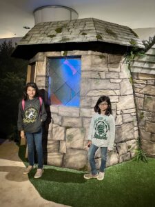 Two young children stand outside Hagrid's Hut at Two young children stand outside Privet Drive at Harry Potter: Magic at Play.