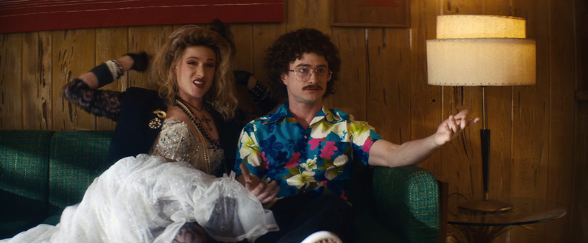 Evan Rachel Wood as Madonna and Daniel Radcliffe as "Weird" Al Yankovic sitting on couch and looking confused in "Weird: The Al Yankovic Story"