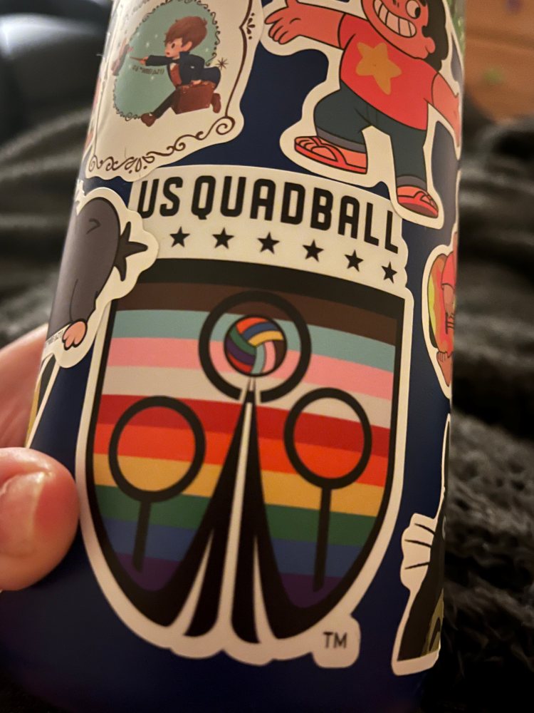 A US Quadball sticker with a background inspired by the Progress Pride Flag is shown on Asher's water bottle.