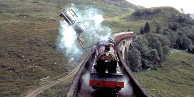A movie still from "Harry Potter and the Chamber of Secrets" where Harry dangles from the flying Ford Anglia over the Hogwarts Express.