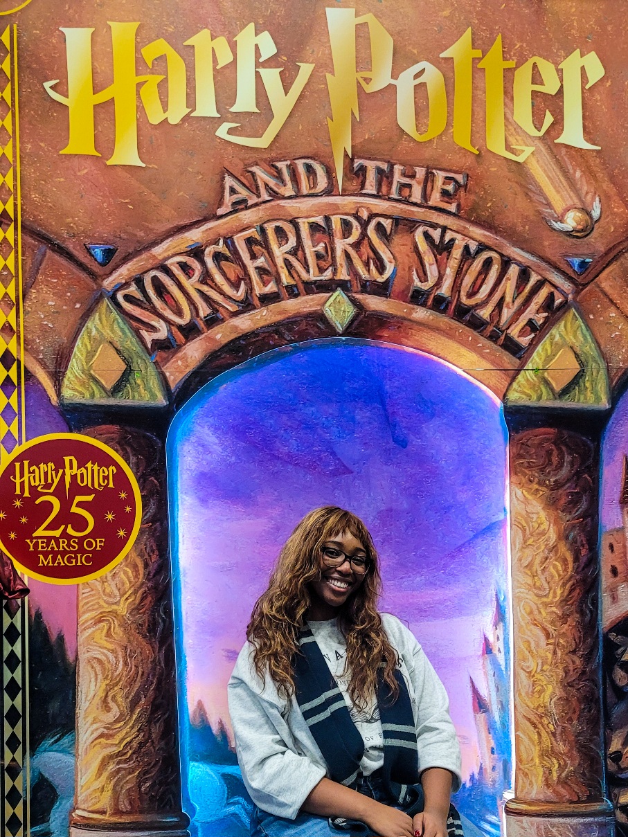 woman standing in front of Sorcerer's Stone 25th anniversary display