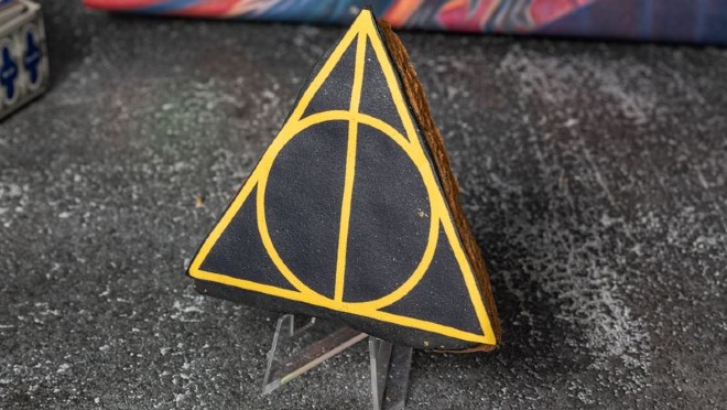 A black triangular cookie emblazoned with the Deathly Hallows sign in gold sits on display.